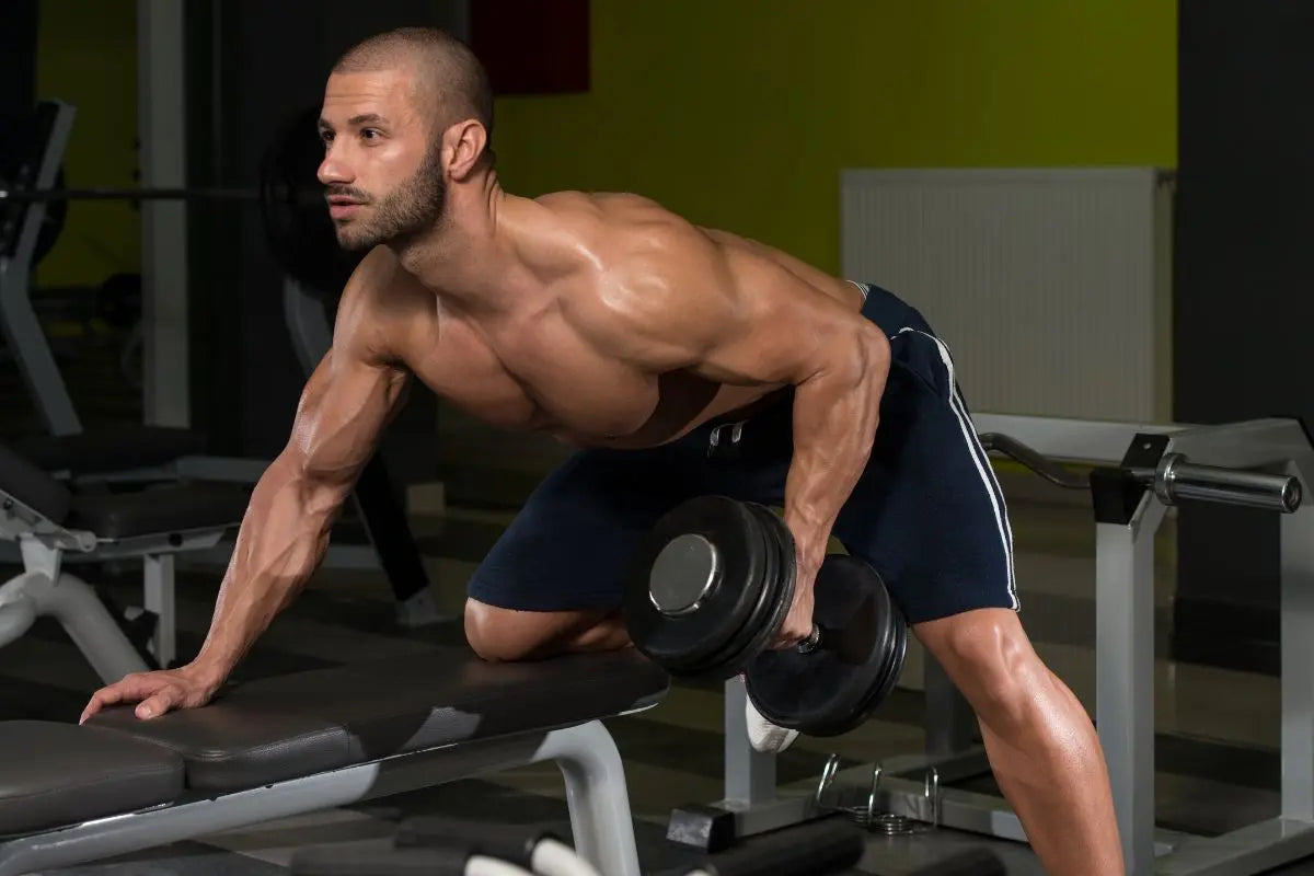 homme qui fait du rowing haltère à la maison avec un banc de musculation pour muscler le dos 